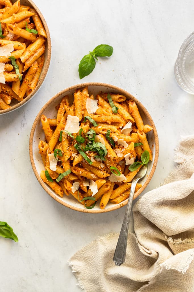 Tomato pesto pasta in a bowl topped with parmesan cheese and sliced basil.