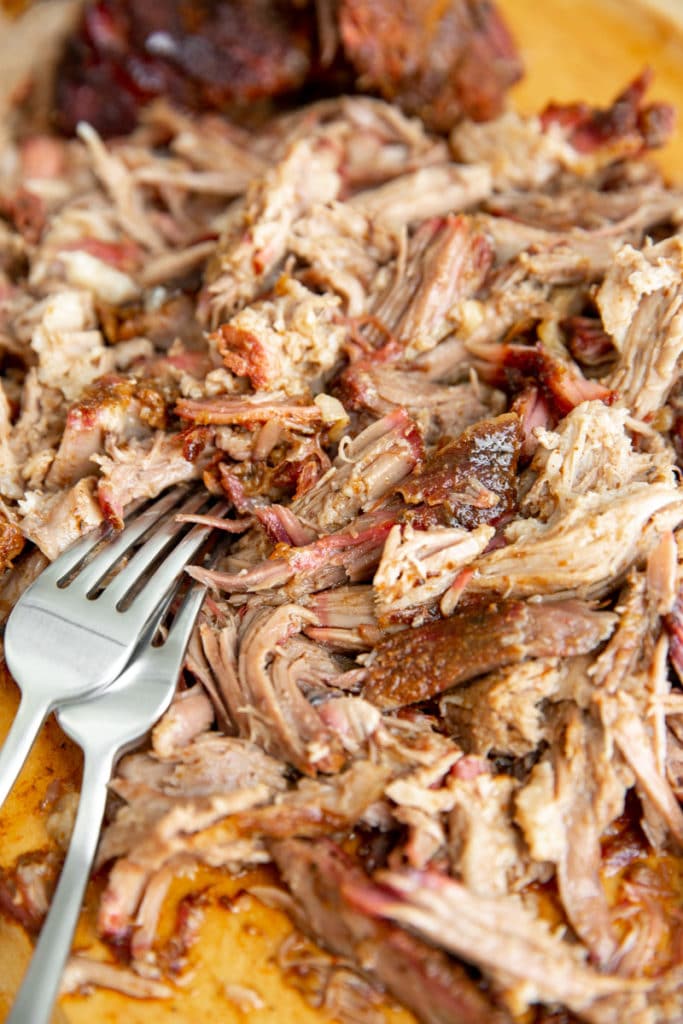 Close up of shredded smoked pork on a cutting board with two forks. 