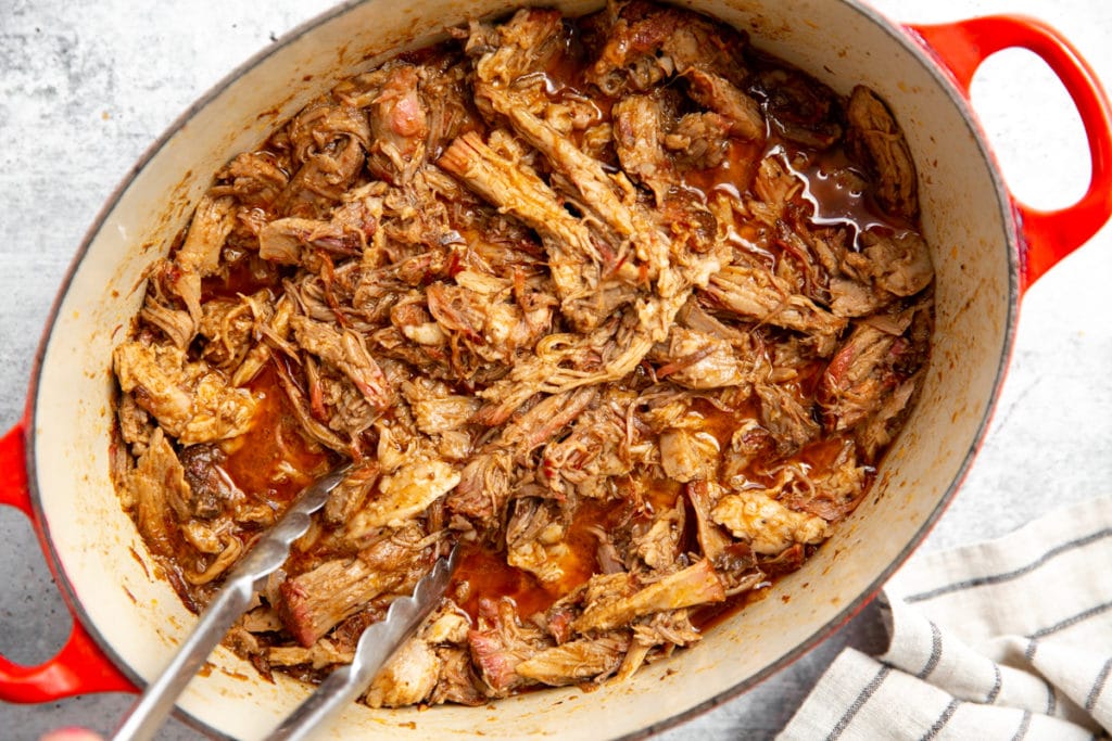 Barbecue pulled pork in a pot with tongs.