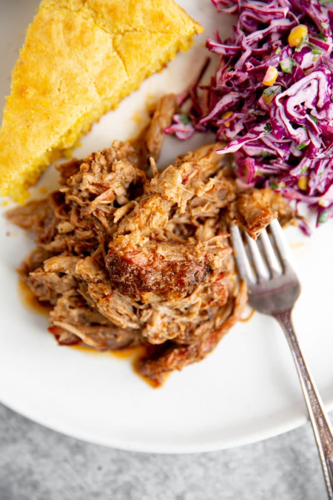 Smoked pulled pork on plate with cornbread and coleslaw alongside.