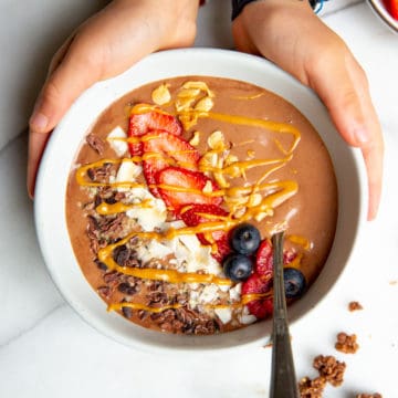 Kids hands wrapped around a chocolate peanut butter banana smoothie bowl.