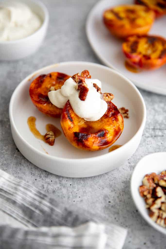 Grilled peaches in a bowl topped with whipped cream and pecans. 