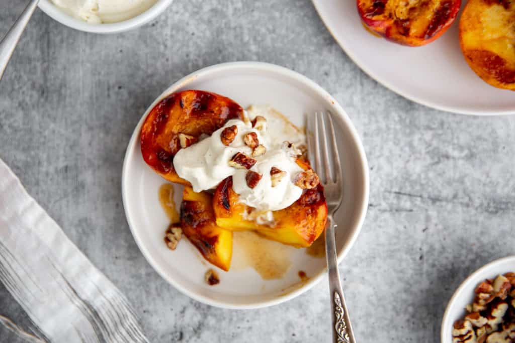 A half eaten bowl of grilled peaches and cream. 