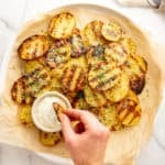 Grilled potatoes on a platter with a hand dipping one into a small bowl of aioli.