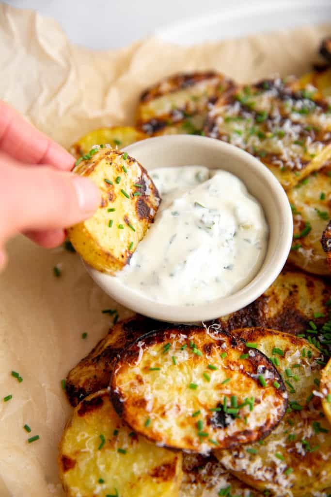 A hand dipping a grilled potato into herbed aioli.