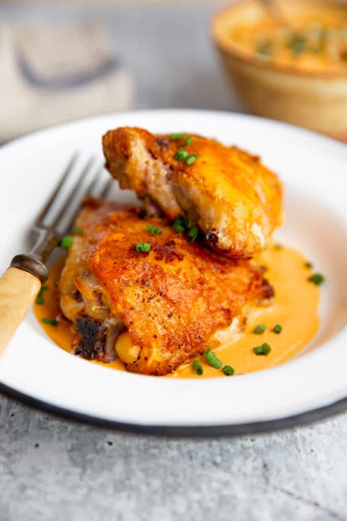 Grilled chicken thighs on a plate over romesco sauce. 