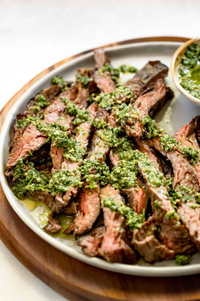 Grilled skirt steak on a platter drizzled with salsa verde.