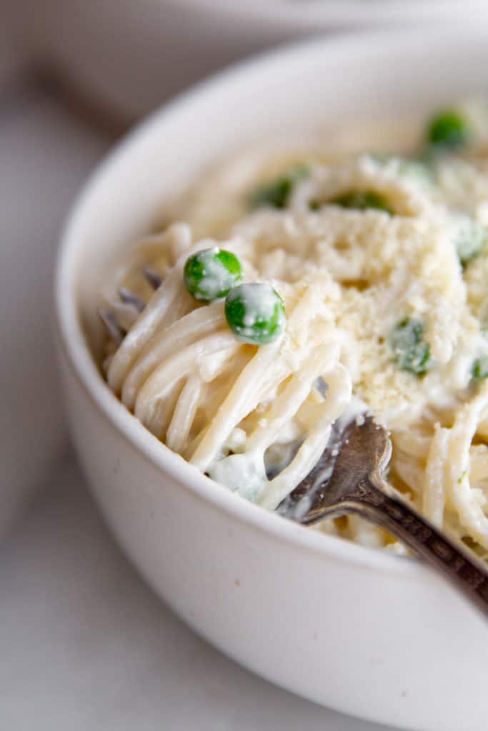 Close-up of a forkful of creamy cottage cheese alfredo pasta with peas. 