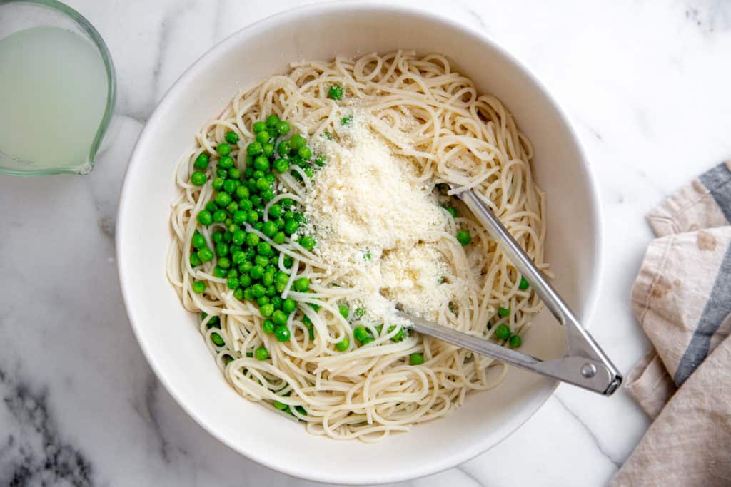 Spaghetti, parmesan and peas in a large bowl with the creamy cottage cheese sauce and tongs.