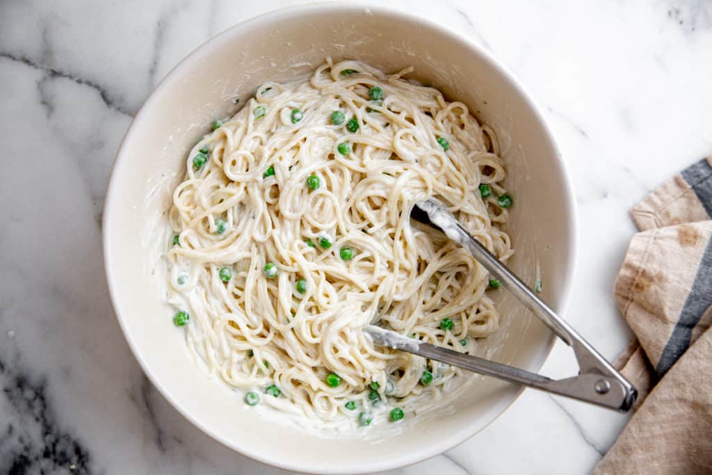 The spaghetti tossed with the creamy sauce in a large bowl with tongs. 