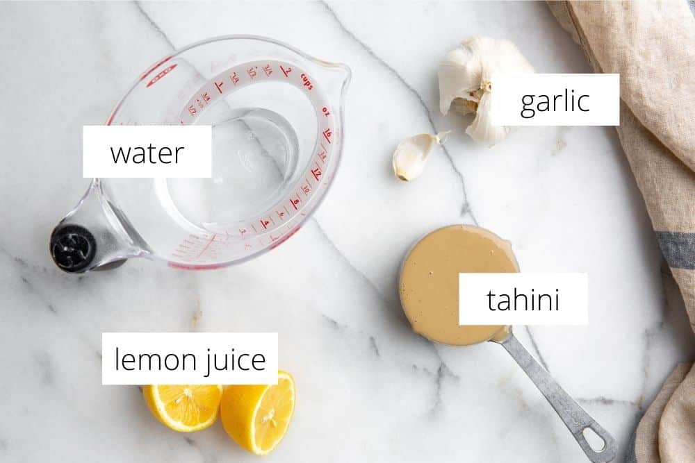 The ingredients for the tahini sauce recipe arranged on a marble surface and labeled.