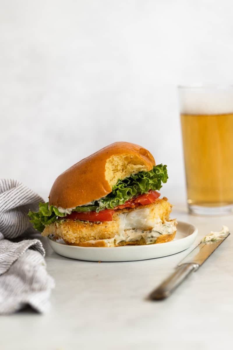 Half-eaten crispy fish sandwich with golden crust, lettuce, and creamy aioli