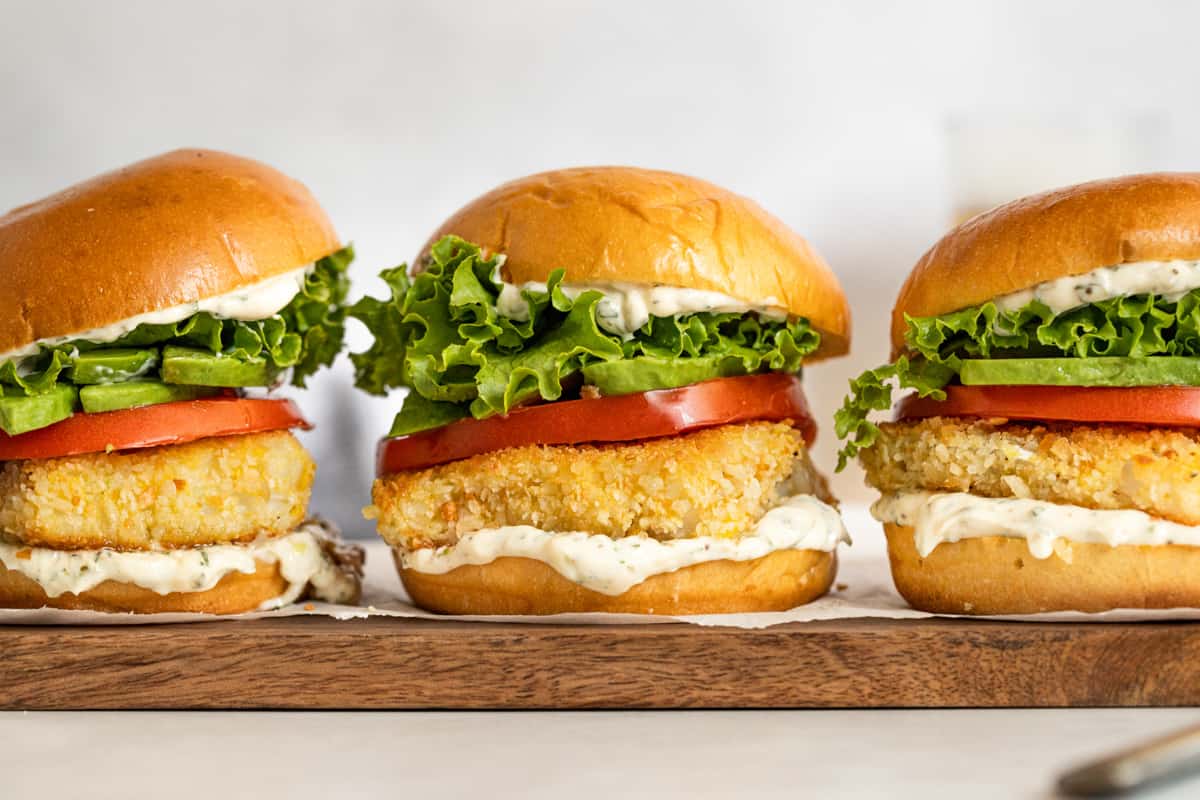 Crispy fish sandwiches with tarragon aioli, lettuce, and tomato on a wooden board