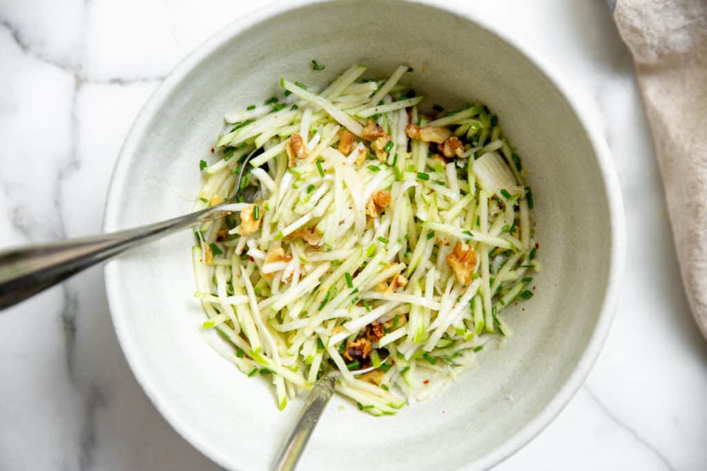 Apple slaw in a serving bowl with serving spoons. 
