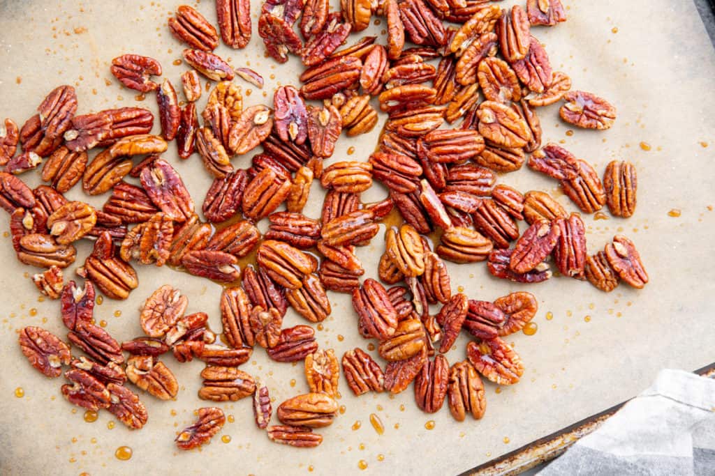 Process shot showing raw pecans on a baking sheet tossed with maple syrup and cinnamon. 