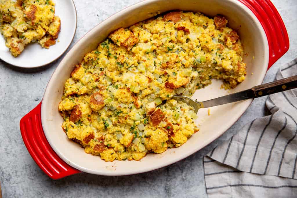 Cornbread stuffing in a baking dish with a serving spoon.
