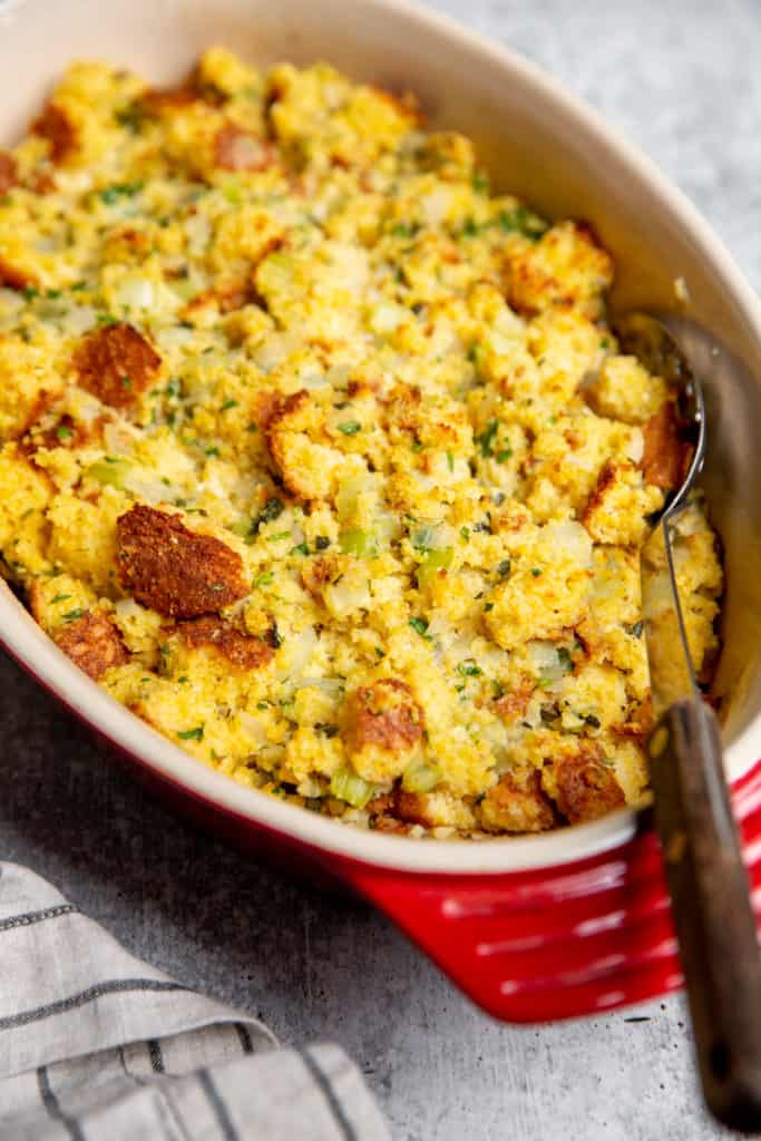 Cornbread dressing in a baking dish with a serving spoon. 
