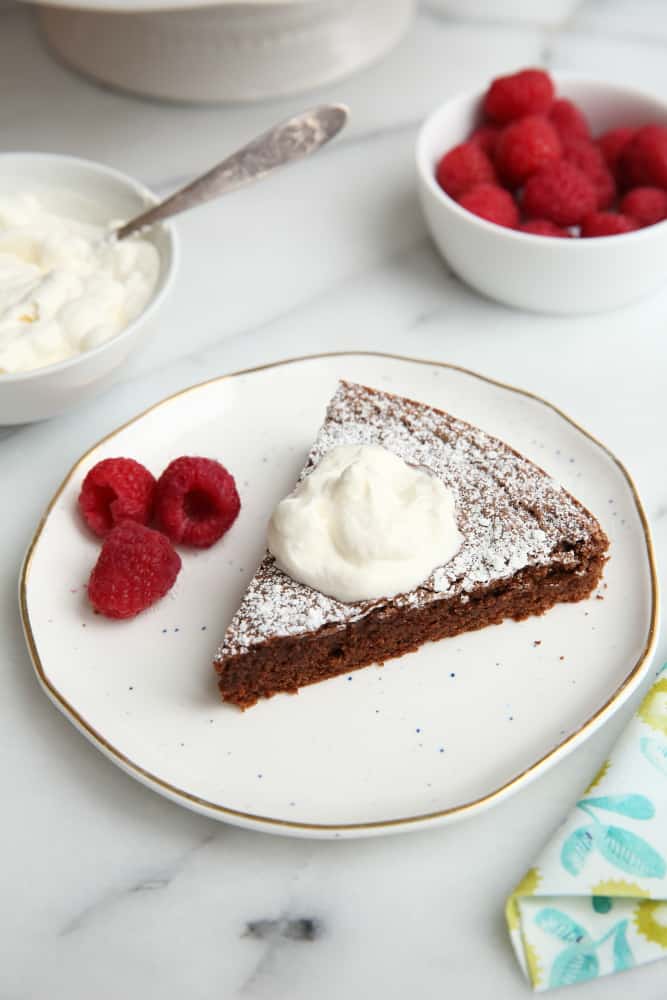Chocolate cake on plate with whipped cream and raspberries.