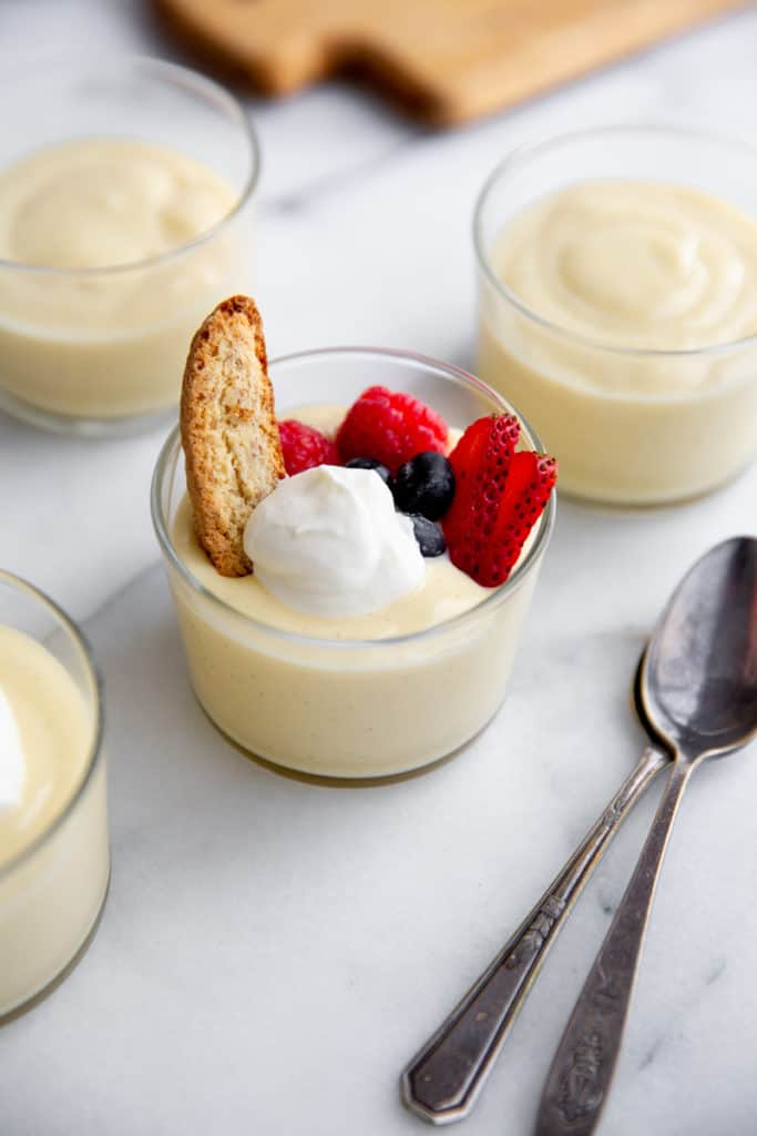 Vanilla pudding in glass jars topped with whipped cream, berries and biscotti. 
