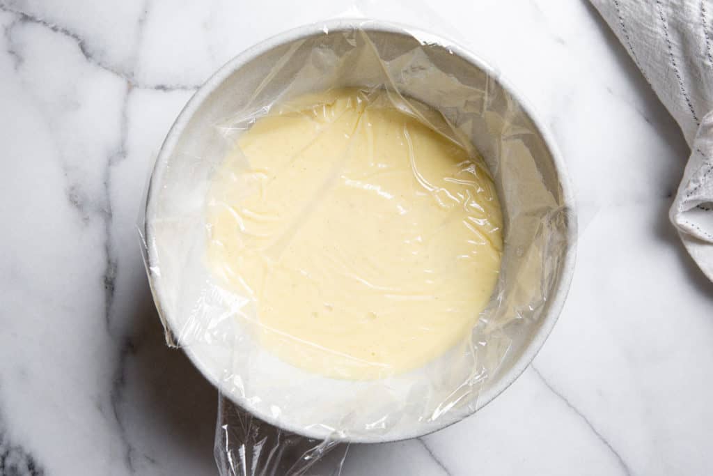 The homemade vanilla pudding in a bowl covered with plastic wrap. 