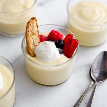 A jar of homemade vanilla pudding topped with whipped cream, berries and a biscotti.