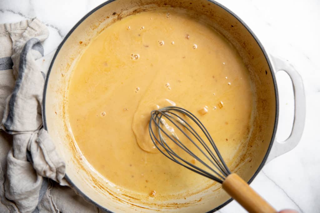 A hand whisking the creamy apple cider pan sauce in a large skillet. 