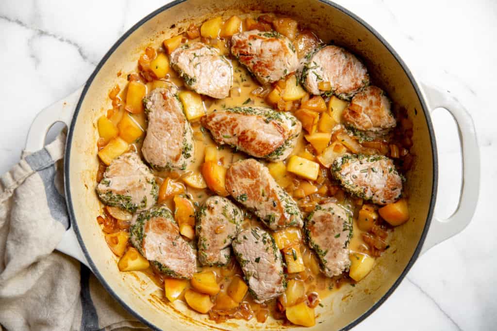 The finished dish with the pork tenderloin and apples in the skillet with the sauce. 