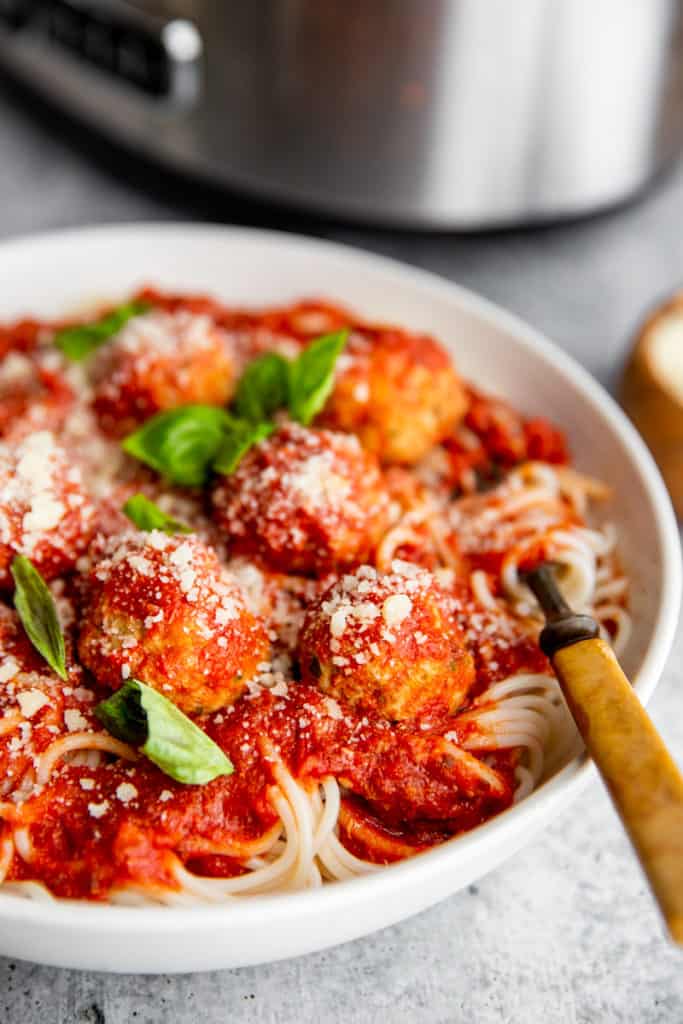 Slow cooker meatballs and tomato sauce over spaghetti in a bowl with a fork. 