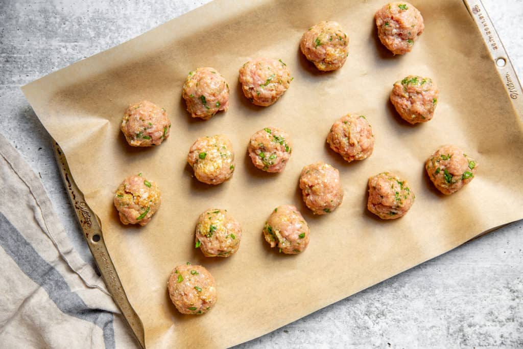 The turkey meatballs arranged on a parchment-lined sheet pan. 