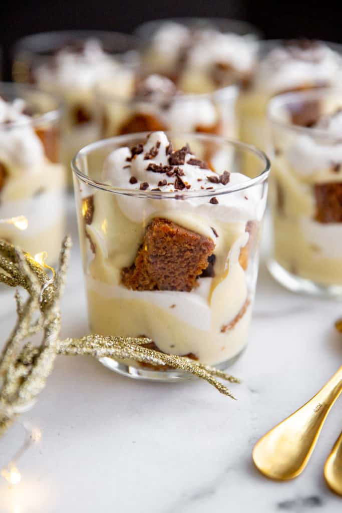 An individual gingerbread trifle in a glass with serving spoons alongside. 