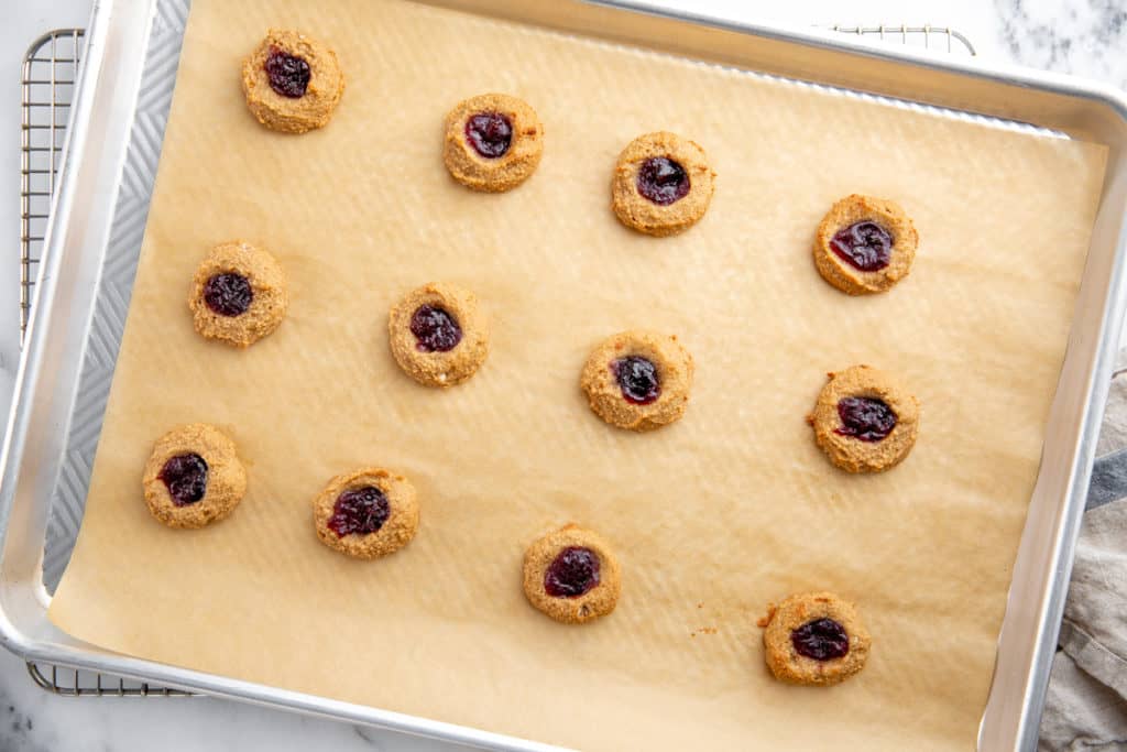 Baked paleo thumbprint cookies on a parchment lined baking sheet. 