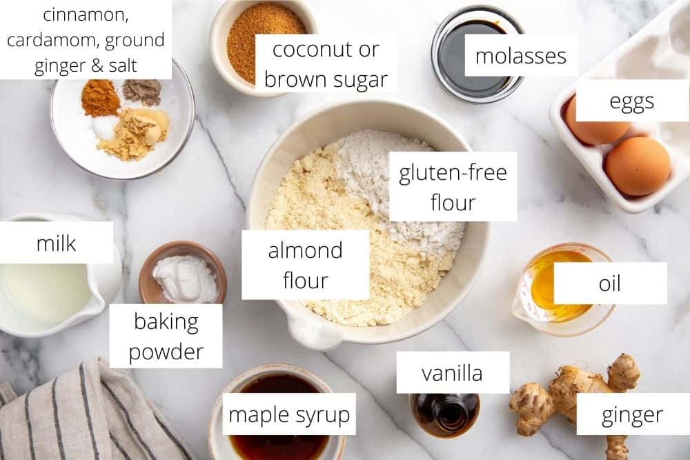 All of the ingredients for the gluten free gingerbread recipe arranged on a marble surface with labels. 