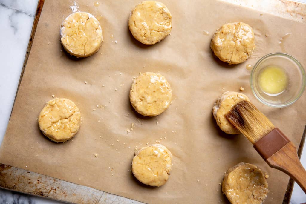 The uncooked biscuits arranged on a parchment-lined baking sheet brushed with melted butter.