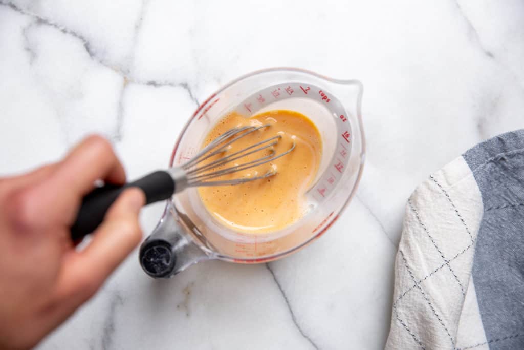 A hand whisking together buttermilk and pumpkin puree.
