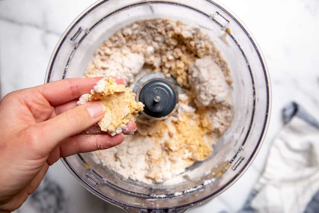 A hand pressing together the biscuit dough with a food processor in the background.