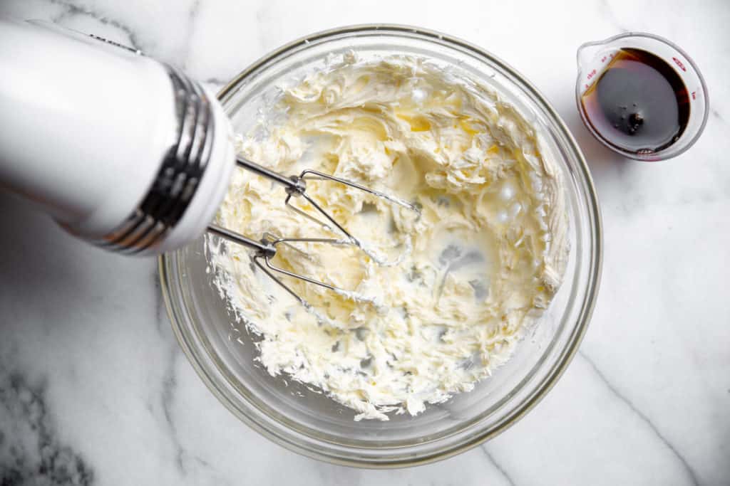 Hand beaters whipping cream cheese in a bowl for the cream cheese frosting.
