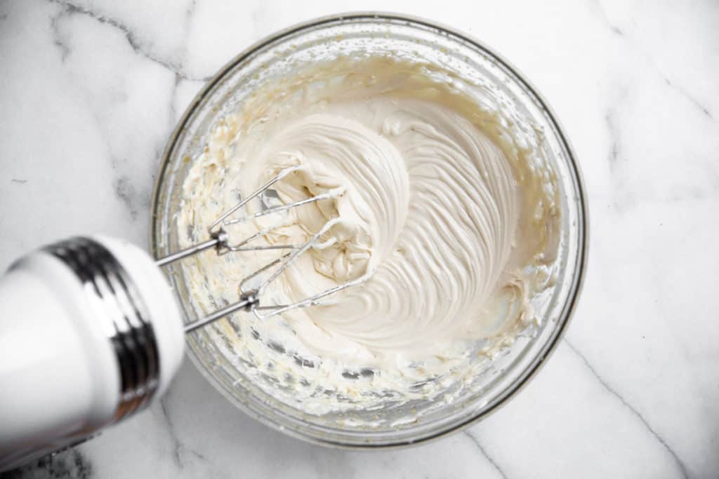 Beaters mixing the maple cream cheese frosting in a bowl. 