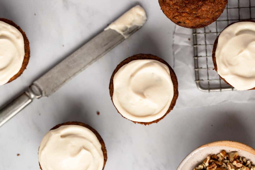Maple cream cheese frosting on muffins with a knife alongside. 
