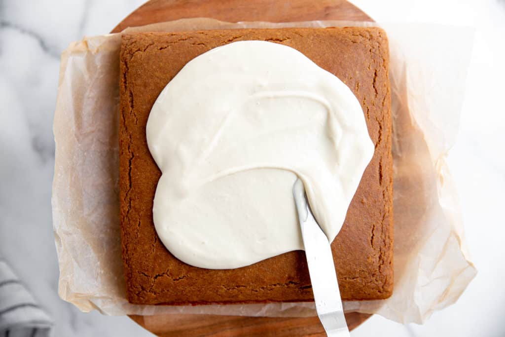 A spatula spreading maple cream cheese frosting over a cake. 