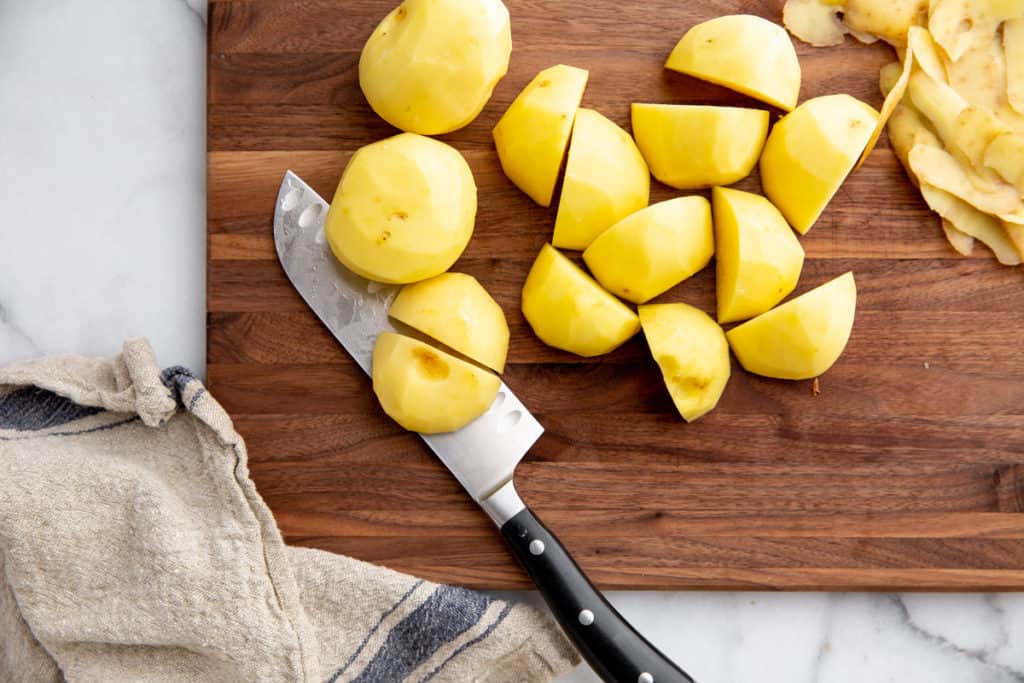 Peeled Yukon gold potatoes cut into chunks on a cutting board. 