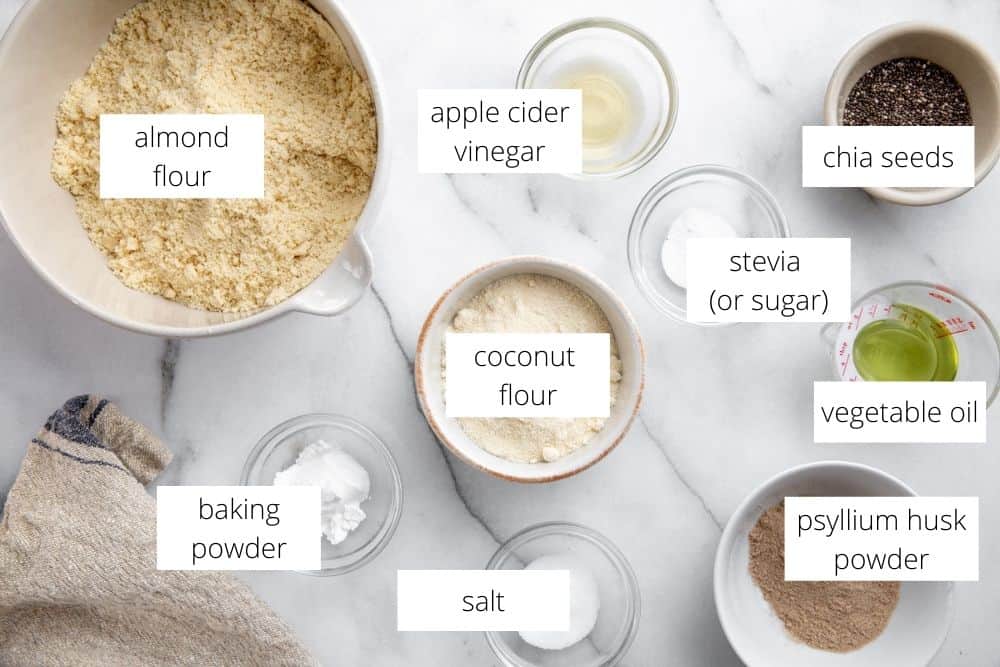 All of the ingredients for the almond flour bread recipe arranged on a marble surface with labels.