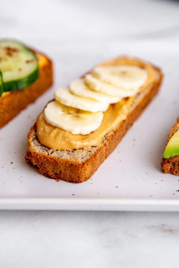 A slice of paleo almond bread topped with nut butter and banana slices. 