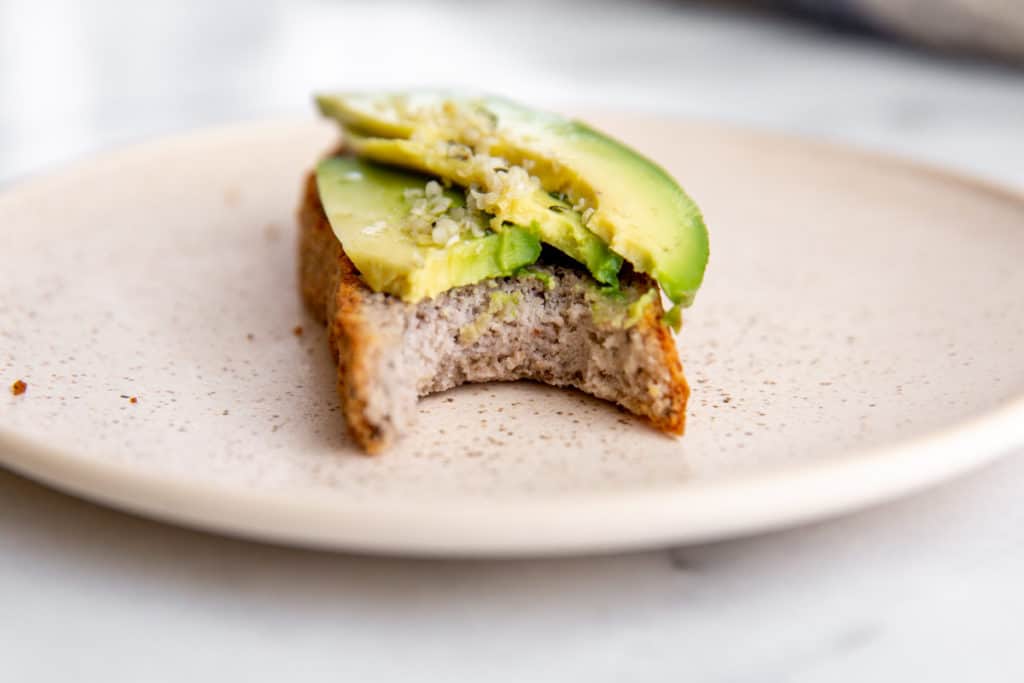 A slice of bread topped with avocado, with a bite taken out.