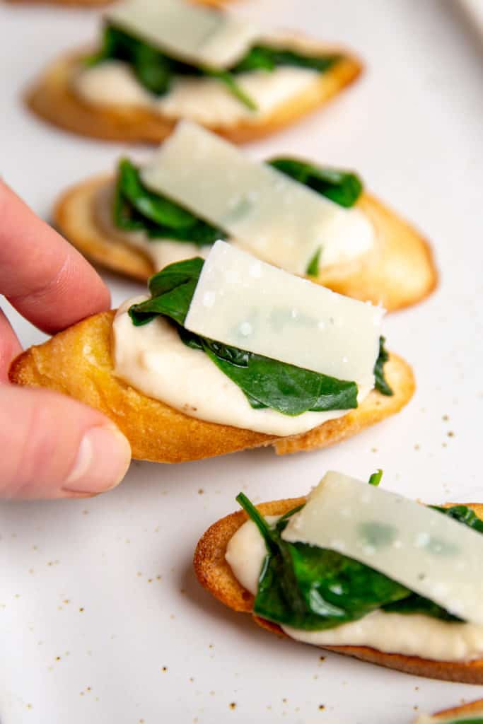 A hand grabbing a white bean crostini off of a serving platter.