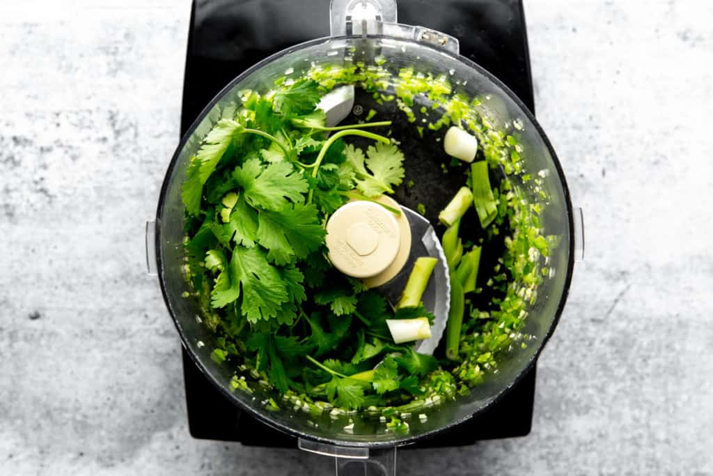 Process shot showing the herbs for the cilantro lime dressing in a food processor. 