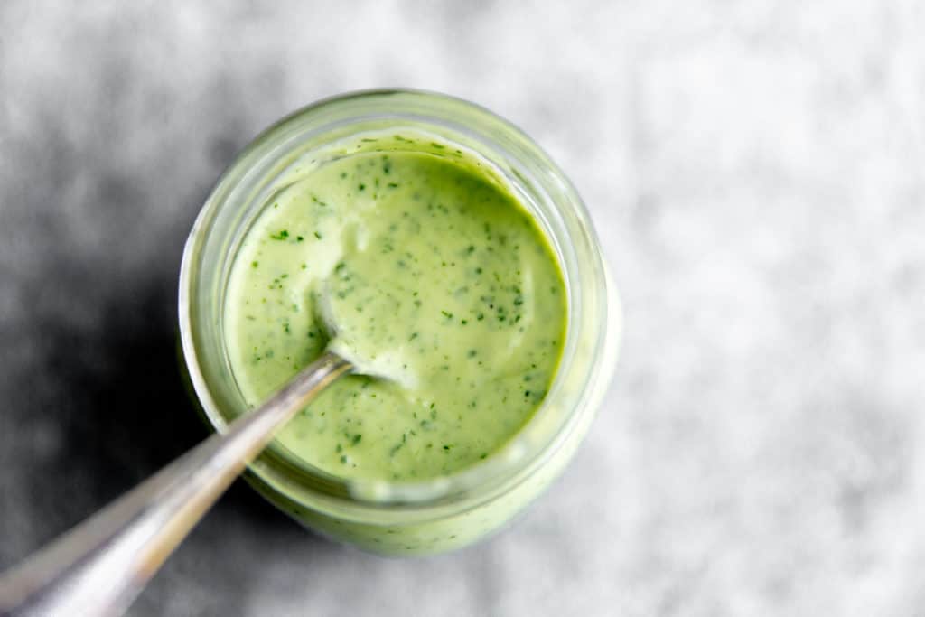 Close up of the cilantro lime dressing in a jar with a spoon. 