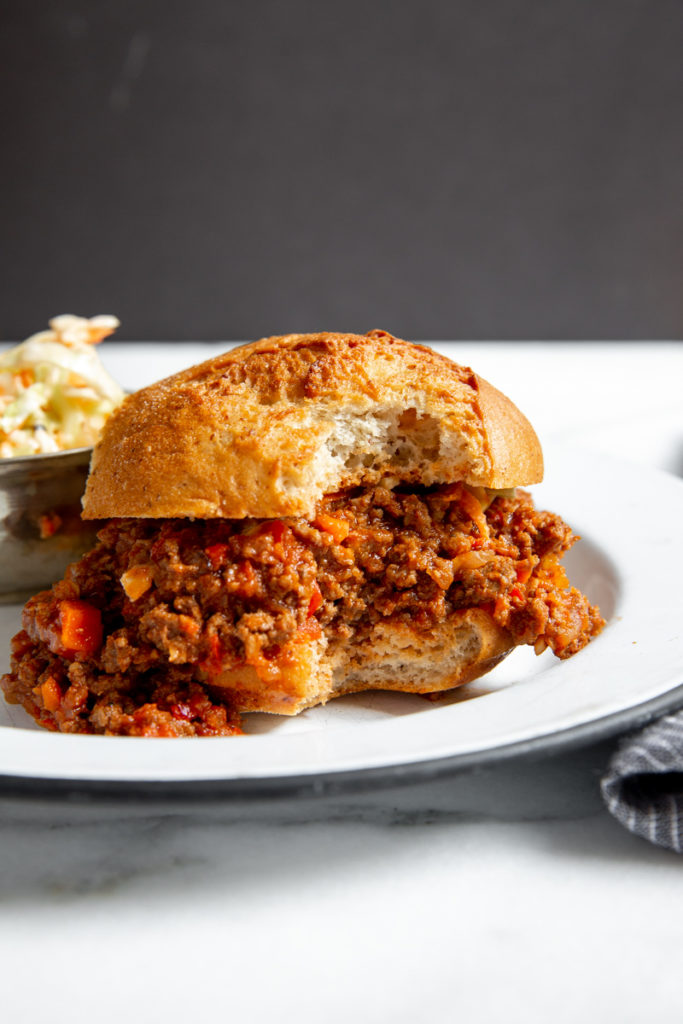 A healthy sloppy joes sandwich on a plate with a bite taken out. 