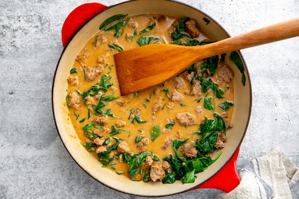The pork and peanut sauce in a skillet with a wooden spoon. 