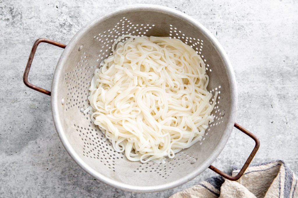 Cooked rice noodles in a colander. 