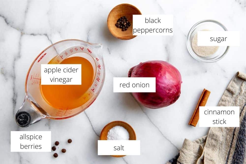 All of the ingredients for the quick pickled red onions recipe arranged on a marble surface with labels. 